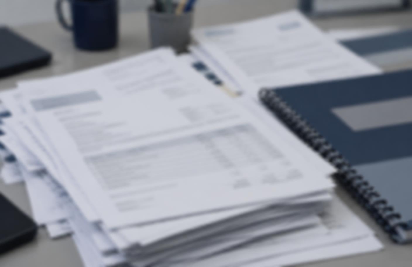 A desk piled with blurred paperwork from separate compliance suppliers